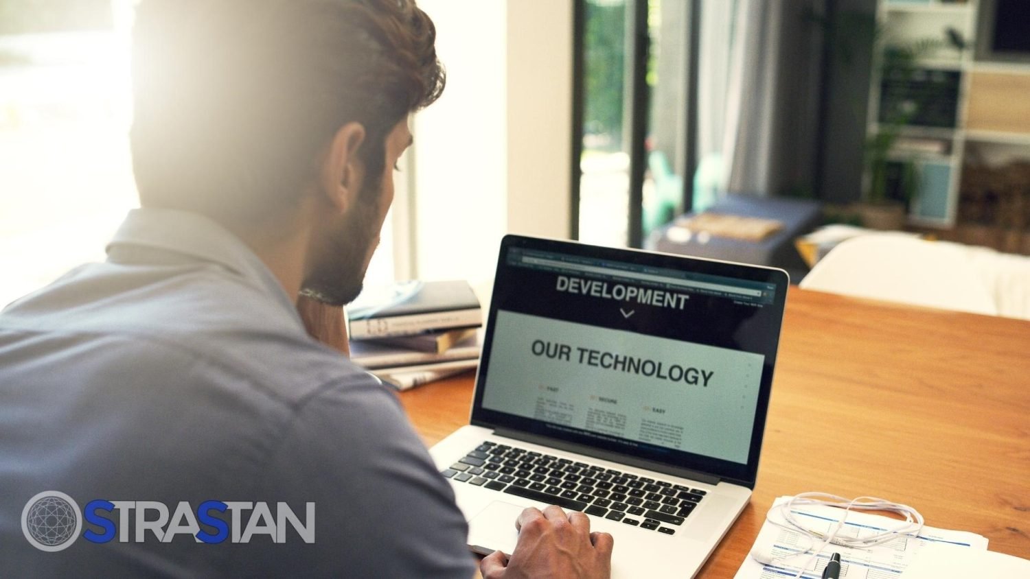 A man working on a laptop with the screen displaying "DEVELOPMENT" and "OUR TECHNOLOGY," representing the process of a business implementing a select custom solution.