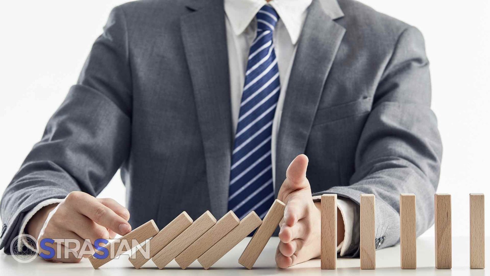 A businessman's hands stopping a line of dominoes from falling, illustrating the proactive support and risk mitigation that comes from thinking a decade forward.