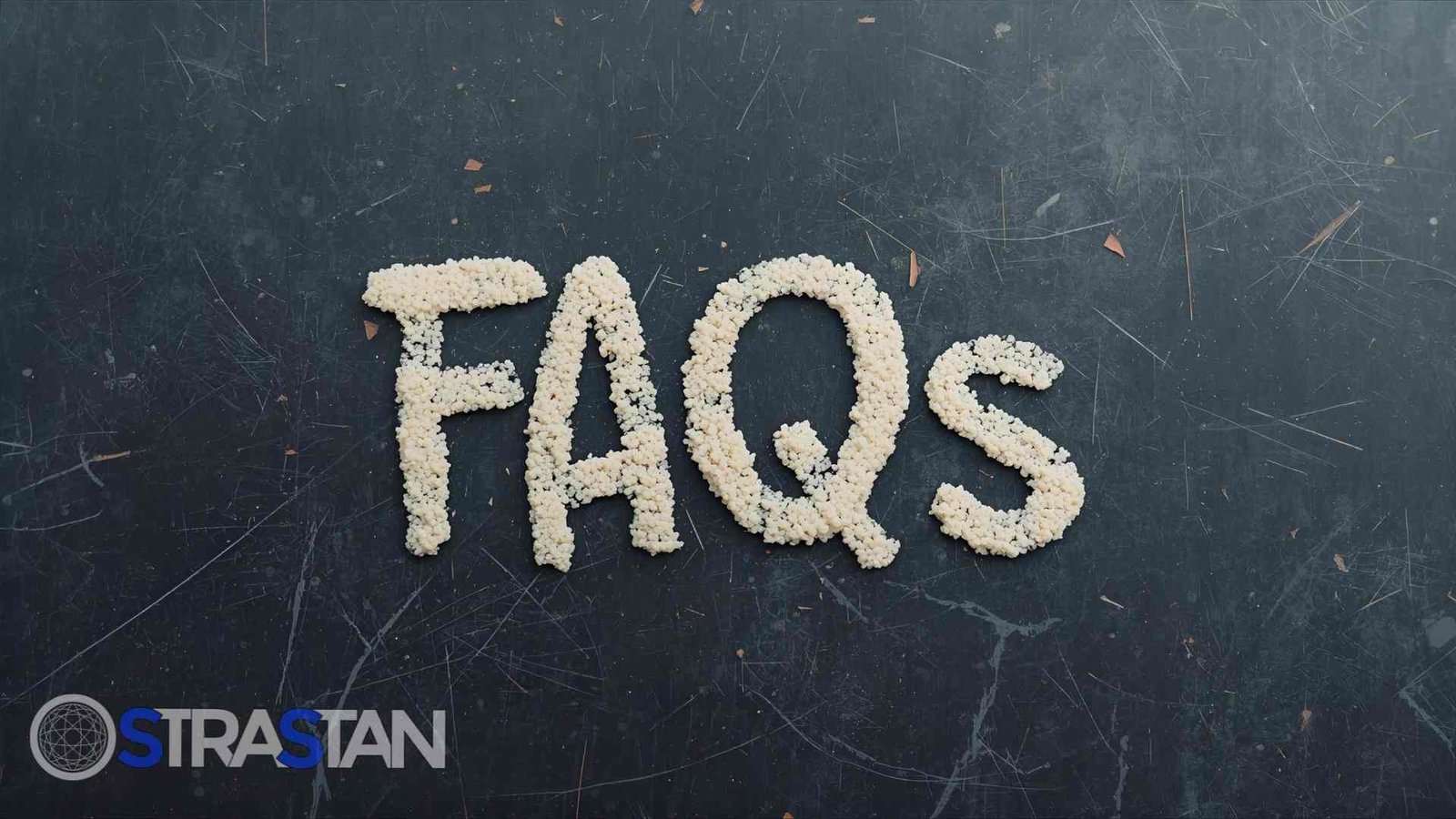 A close-up of the word "FAQs" spelled out in small, white, granular material on a dark, textured background, representing common questions addressed in an FAQs guide.