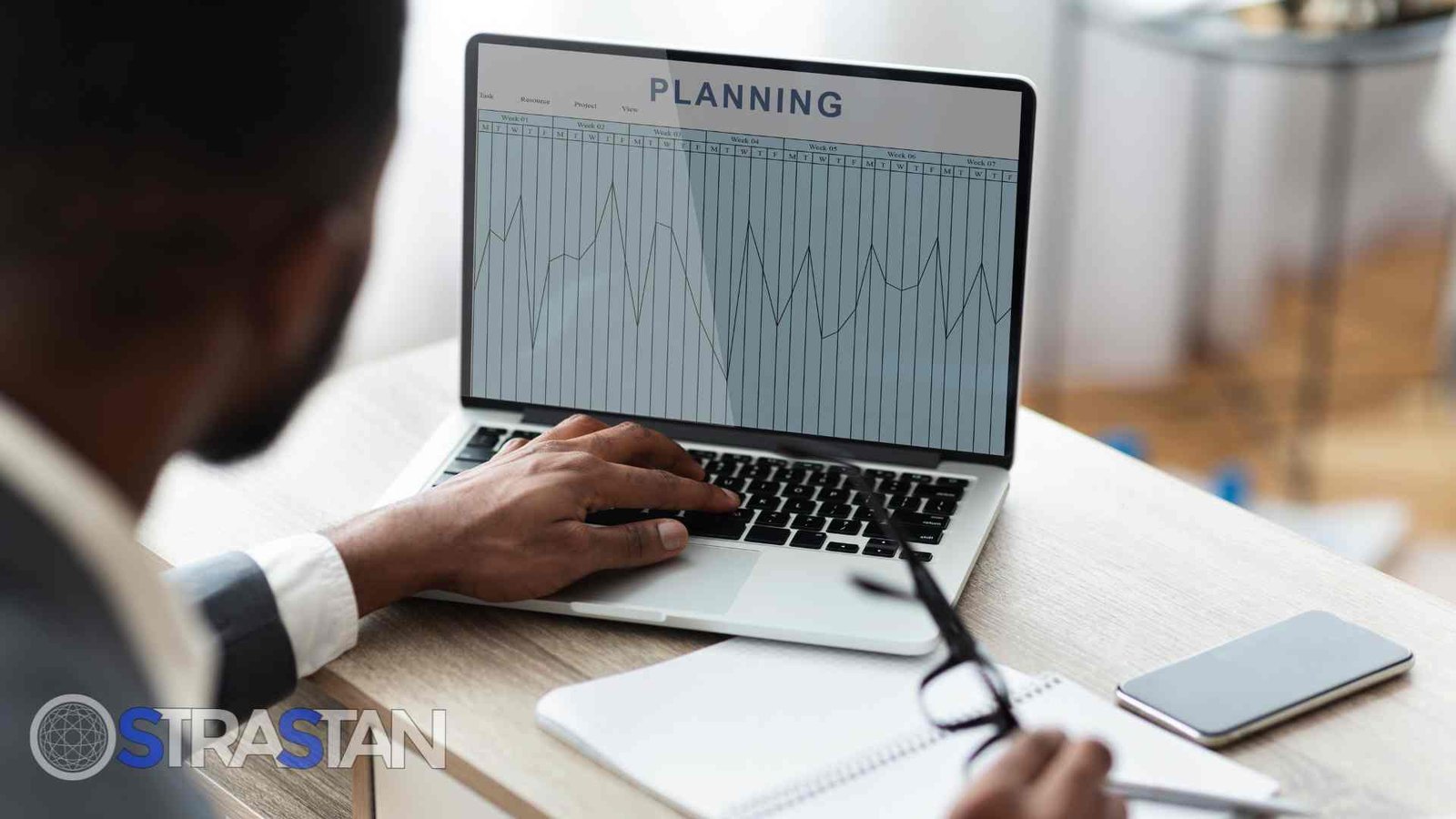 A person actively engaged in budget planning on a laptop, with a chart labeled "PLANNING" displayed.