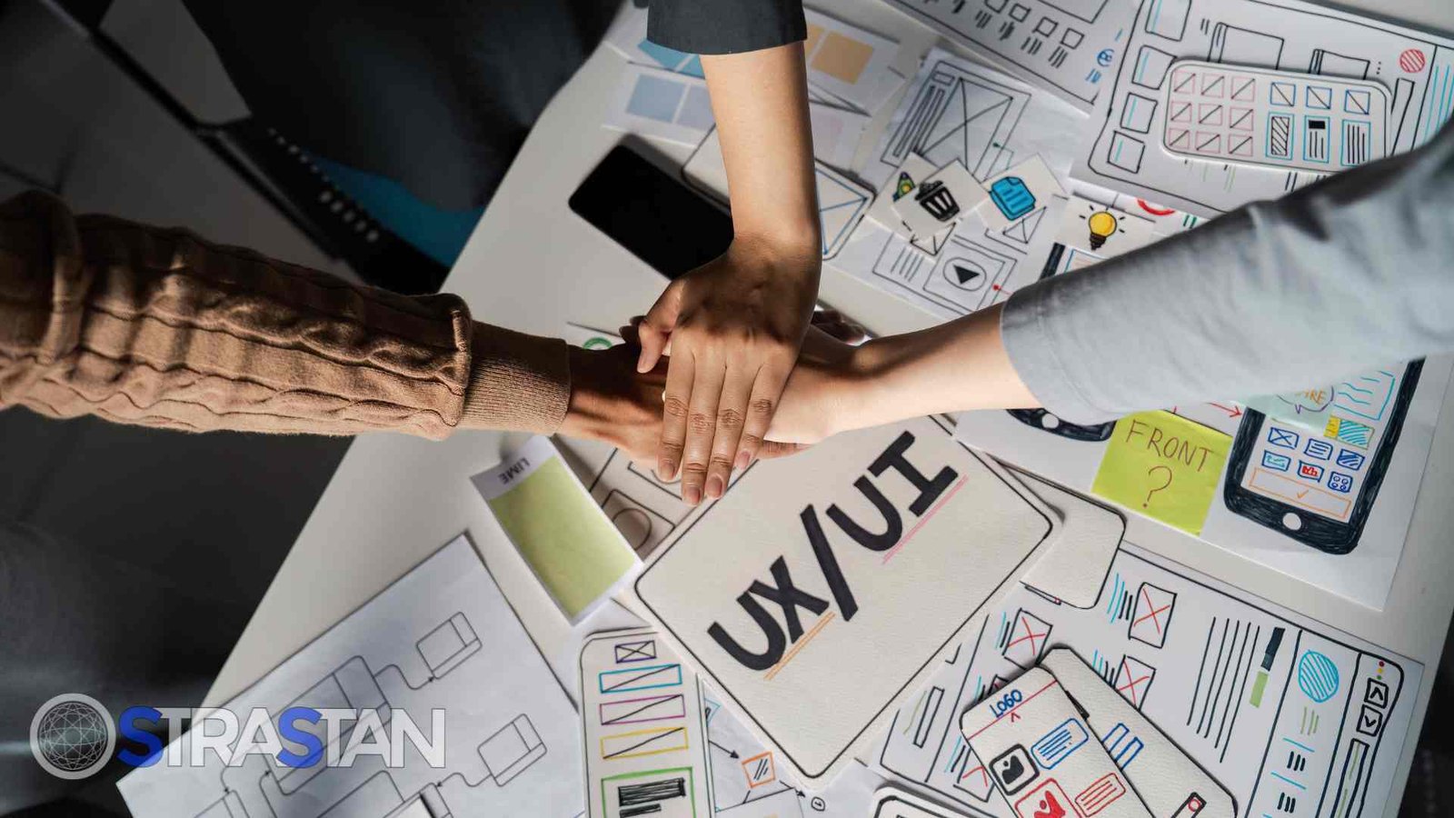 Three pairs of hands stacked on top of a table with UI/UX design documents, symbolizing teamwork and commitment to the design process.