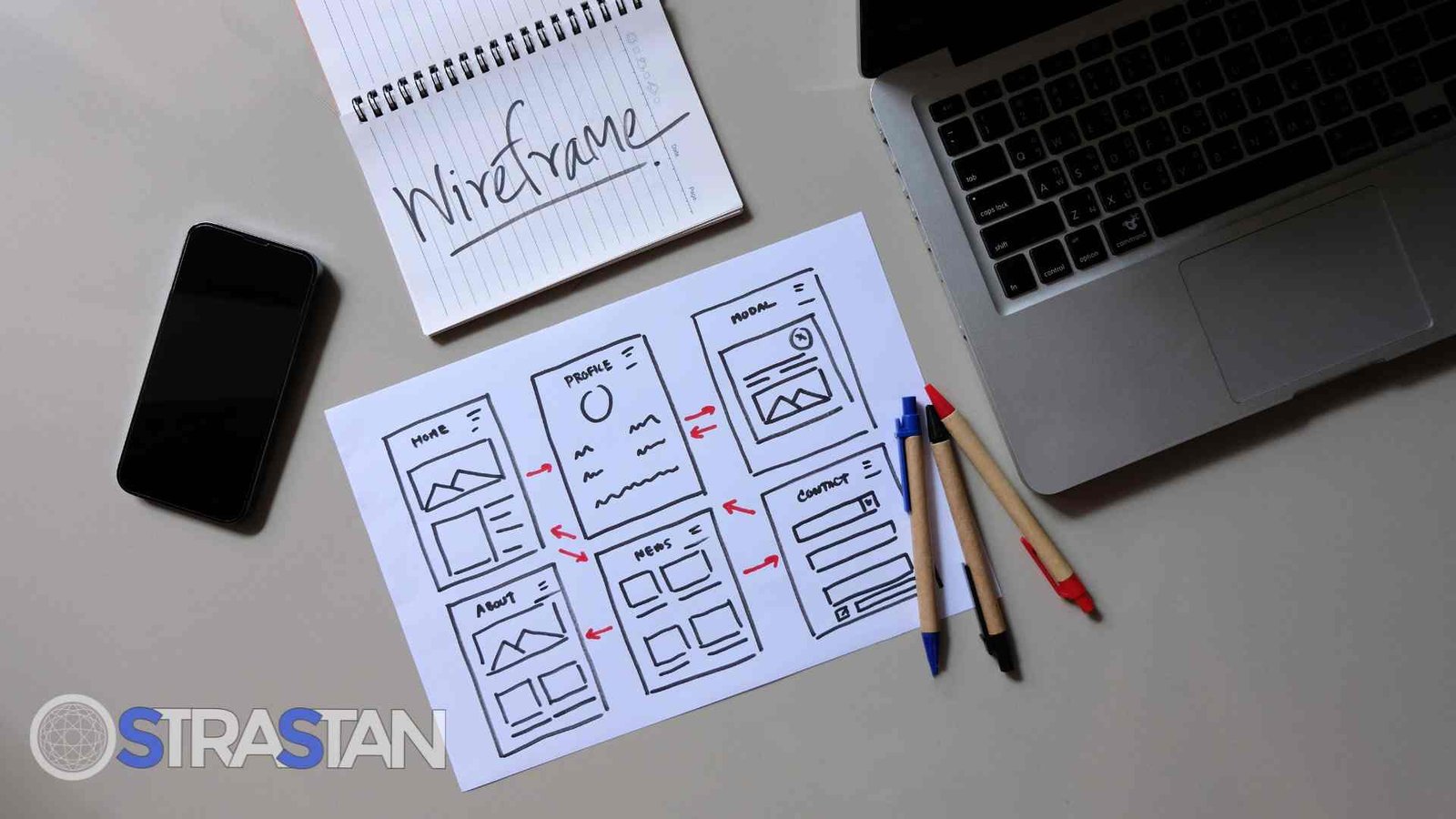 A flat-lay image of a desk showing an app building guide in the form of hand-drawn wireframes, a notebook, and a laptop.