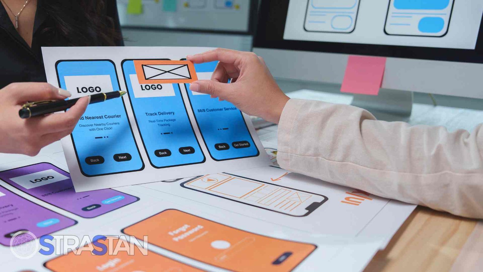 Two people are reviewing and arranging physical mockups of a mobile app's interface screens, demonstrating a collaborative step in the app building guide.